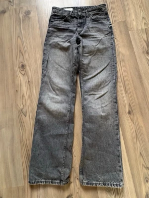 Grå raka jeans - Säljer ett par grå jeans med rak passform. Klassisk femficksmodell med knapp och dragkedja framtill. Jeansen har en tvättad look och är tillverkade i denim. Perfekta för en avslappnad och trendig stil.