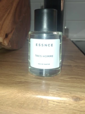 ESSNCE Tres Homme Eau de Parfum - ESSNCE Tres Homme Eau de Parfum kommer i en stilren, genomskinlig glasflaska med svart lock och vit etikett. Doften är maskulin och modern, perfekt för dig som vill ha en fräsch signaturparfym. Flaskan har en enkel och elegant design.                                