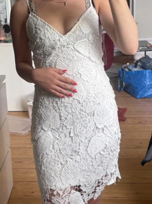 Vit spetsklänning med v-ringning - Säljer en vit kort klänning med v-ringning och smala axelband. Klänningen har ett vackert spetsmönster med blommiga detaljer. Perfekt för sommarens alla tillfällen!🤍🙌🏼🤩