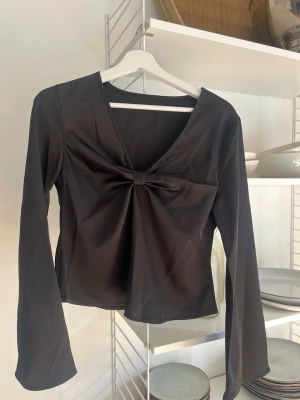 Svart långärmad topp med rosett - Snygg svart långärmad topp med v-ringning och en dekorativ rosettdetalj framtill. Aldrig använd då den tyvärr inte är min stil, skriv för fler bilder💕