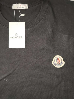 Svart Moncler t-shirt i bomull - Snygg svart t-shirt från Moncler med klassisk rund hals och korta ärmar. Tillverkad i mjuk bomull och pryds av Monclers ikoniska logotyp på bröstet. Perfekt för dig som vill ha en stilren och exklusiv look.