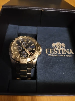 Festina Klocka - Använd men i bra skick. Sliver med en blåsvart bakgrund och tre extra visare som visar dag, datum och månad.