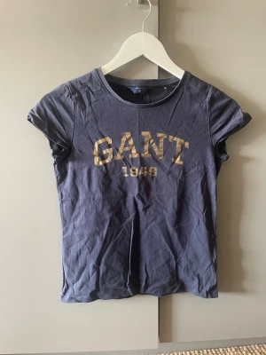 Mörkblå GANT t-shirt med tryck - Snygg mörkblå t-shirt från GANT med guldfärgat tryck framtill där det står 'GANT 1949'. Klassisk rund halsringning och korta ärmar. 