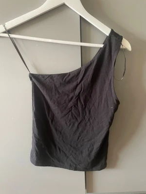 Svart oneshoulder topp Gina Tricot - Säljer en svart oneshoulder topp från Gina Tricot. Toppen har en smal axelrem på ena sidan och är ärmlös på andra, vilket ger en snygg asymmetrisk look. Tillverkad i mjukt bomullsmaterial som känns skönt mot huden.