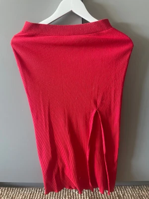 Röd ribbad kjol med slits  - Säljer en snygg röd ribbad långkjol från hm  i storlek XS. Kjolen har en markerad midja och en cool slits framtill som ger extra edge. Tillverkad i mjuk polyesterblandning som sitter skönt och följer kroppen.