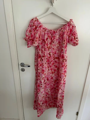 Blommig offshoulder midiiklänning L - Säljer en lång offshoulder klänning med blommigt mönster i rosa, rött och vitt. Klänningen har puffiga korta ärmar och smock över bysten för en bekväm passform. Perfekt för sommarens alla tillfällen!