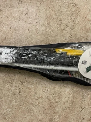 Badmintonset i väska - Komplett badmintonset med två racketar, nät, stolpar och tillbehör i en svart och transparent bärväska. Perfekt för att spela utomhus eller ta med till parken. Innehåller även instruktioner och markeringslinjer.