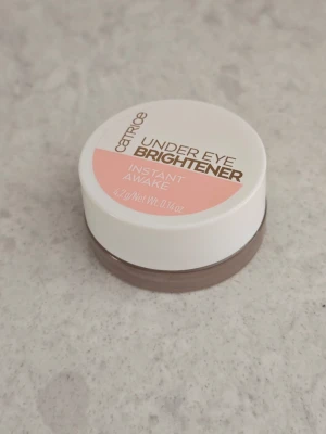 Catrice Under Eye Brightener concealer - Catrice Under Eye Brightener Instant Awake är en krämig concealer i en liten rund burk. Färgen är ljusrosa och formulan är lätt att applicera under ögonen för att ljusa upp och dölja mörka ringar. Perfekt för en piggare look och enkel att ta med i väskan.