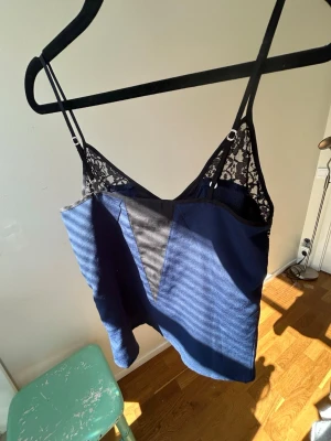 Blå linnetopp med spetsdetaljer - Snygg blå linnetopp med svarta spetsdetaljer upptill och tunna axelband. Toppen har en v-formad insats framtill i svart tyg och spets längs ryggen. Perfekt för dig som vill ha en trendig och stilren look🥂💗