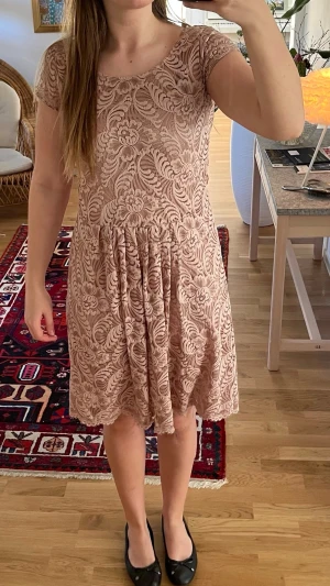 Spetsklänning med öppen rygg - Söt kortklänning med blommigt spetsmönster och rund halsringning. Klänningen har korta ärmar och en snygg öppen ryggdetalj. Kjolen är lätt utställd och materialet känns mjukt och följsamt. Perfekt för dig som gillar romantisk stil!