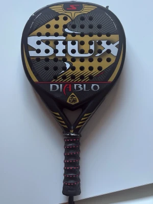 Siux Diablo padelracket svart/guld - Säljer ett Siux Diablo padelracket i svart och guld med tydlig logga och text. Legat hemma ett bra tag, använt hyfsat mycket. Nypris ca. 1900-2400. Köptes för 3 årsen 