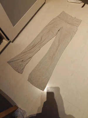 Gråmelerade utsvängda leggings/ Yogapants - Säljer ett par gråmelerade leggings med utsvängda ben och hög midja. Mjukt och stretchigt material som sitter skönt på kroppen. Perfekta för en avslappnad och trendig look. De har dock lite färg vid benet men aja..