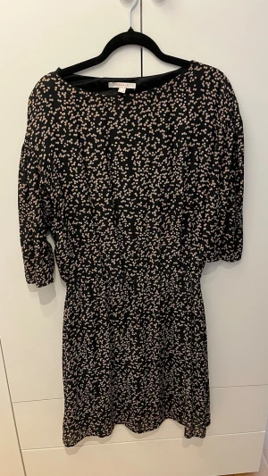 Prickig klänning  - Kortklänning från Esprit i svart med små beige prickar över hela tyget. Klänningen har rund halsringning, resår i midjan och halvlånga ärmar. Tillverkad i ett mjukt och lätt material som ger en skön passform.
