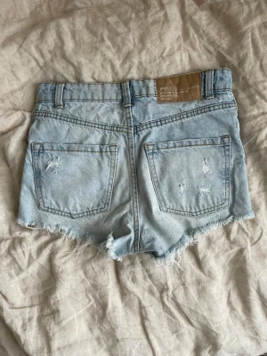 Ljusblå denimshorts - Säljer ett par ljusblå denimshorts med fransiga kanter och slitna detaljer både fram och bak. Klassisk femficksmodell med bälteshällor. Perfekta för varma dagar och en avslappnad stil. Skriv om ni har andra frågor!🥰