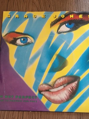 Grace Jones vinylsingel - Säljer en vinylsingel med Grace Jones, låten 'I'm Not Perfect (But I'm Perfect For You)'. Omslaget har ett färgstarkt konstverk med blå, gula och lila toner. Baksidan listar låtarna och har detaljer om produktionen. Perfekt för dig som gillar 80-talsmusik och samlar på vinyl.