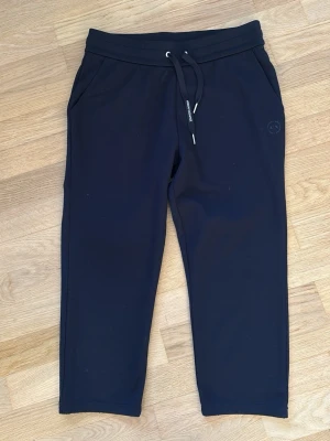 Svarta mjukisbyxor Armani Exchange - Snygga svarta mjukisbyxor från Armani Exchange med dragsko i midjan och två sidofickor. Byxorna har en diskret logga på benet och är gjorda i mjukt, stretchigt material som känns riktigt skönt mot huden. Perfekta för en avslappnad och trendig look. Midja: 38 cm, ytterlängd: 83 cm, innerbenslängd: 49 cm