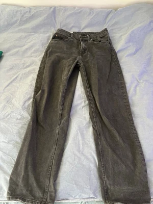 Svarta raka jeans med vintage-look - Säljer ett par svarta jeans med rak passform och klassisk femficksdesign. Jeansen har en snygg vintage-tvättad look och är tillverkade i denim. Perfekta för dig som gillar en avslappnad och tidlös stil.