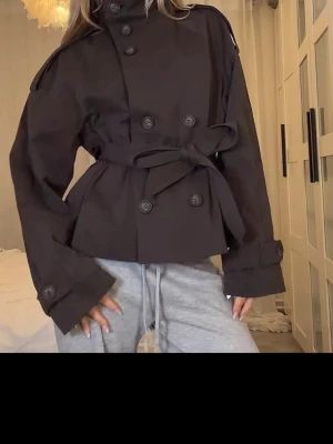 trenchcoat från Bershka  - Populära jackan från Bershka Snygg brun trenchcoat  Jackan har stora knappar, axelklaffar och justerbara ärmslut. Perfekt för dig som vill ha en trendig och stilren look. Helt ny med prislapp