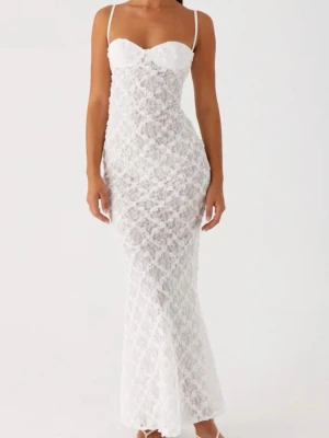 Vit spetsklänning med smala axelband - Supersnygg lång vit klänning i spets med smala axelband och figurnära passform. Klänningen har en v-ringad byst och är helt täckt i ett romantiskt spetsmönster. Perfekt för dig som vill sticka ut med en elegant och feminin look.