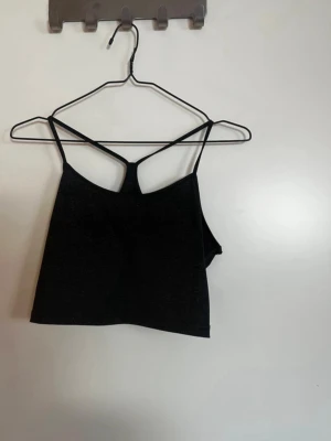 Svart crop top med tunna axelband - Snygg svart crop top med tunna axelband och racerback-design. Toppen är gjord i ett mjukt, stretchigt material som känns bekvämt mot huden. Perfekt att matcha med höga jeans eller kjol för en trendig look. Rök och djurfritt hem. Pruta gärna!🌸