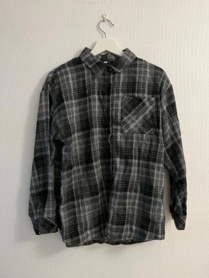 Svart och grå rutig skjorta - Klassisk rutig skjorta i svart och grå toner med lång ärm och bröstficka. Skjortan har knappar framtill och en avslappnad passform, perfekt för en chill och stilren look. Tillverkad i mjukt bomullstyg som känns skönt mot huden.