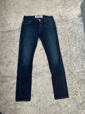 Mörkblå jacob cohen jeans herr - Snygga mörkblå jacob cohen jeans herr med klassisk femficksdesign och kontrastsömmar. Jeansen har en något tvättad look och är tillverkade i mjuk denim med stretch för extra komfort. Perfekta för en avslappnad och trendig stil. Storlek: 31