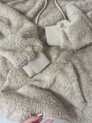 Beige teddyjacka med huva - Supermjuk teddyjacka i beige med huva och långa ärmar. Jackan har ribbade muddar vid handlederna och dragsko i huvan för extra mysfaktor. Perfekt för dig som vill ha en varm och chill look.