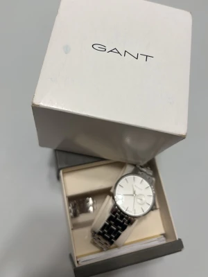 Silverfärgad klocka från GANT - Stilren klocka från GANT med silverfärgat armband i metall och vit urtavla. Klassisk design med länkarmband och minimalistiska detaljer. Perfekt accessoar för dig som gillar en clean och tidlös look.