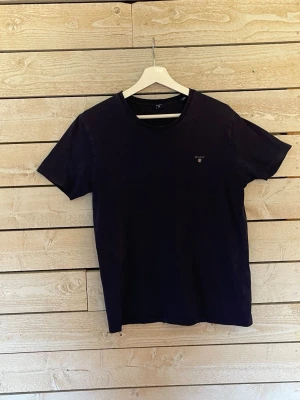 Mörkblå t-shirt från Gant - En stilren mörkblå t-shirt från Gant med liten logga på bröstet. Klassisk rund halsringning och korta ärmar. Tillverkad i mjuk bomull för skön känsla och enkel passform. Perfekt till jeans eller shorts.