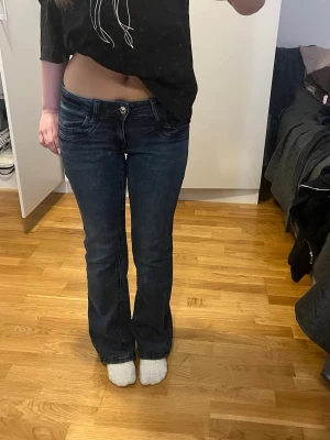 Mörkblå bootcut jeans - Säljer ett par mörkblå bootcut jeans med låg midja och klassiska fem fickor. Jeansen har en snygg tvätt och är tillverkade i stretchigt denimtyg för skön passform. Perfekta till sneakers eller boots och ger en retrovibe till din outfit. storlek 164!