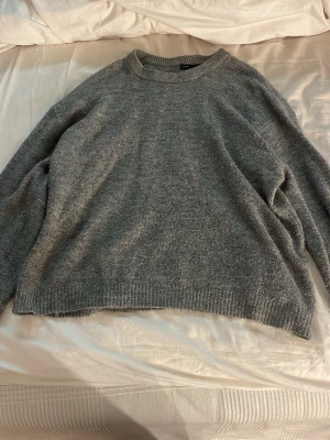 Grå stickad tröja  - Mysig grå stickad tröja med rund hals och avslappnad passform. Tröjan har ribbade muddar vid ärmslut och nederkant, perfekt för lager på lager och en chill look.