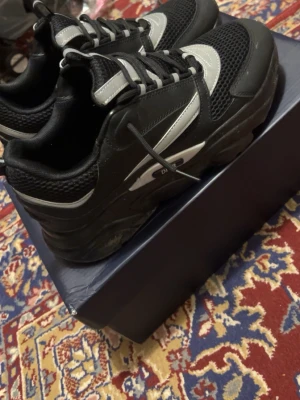 Svarta chunky sneakers med meshdetaljer - Säljer ett par svarta sneakers med vita och grå detaljer. Skorna har chunky sula, meshpartier för extra ventilation och snörning framtill. Snygg sportig look med kontrasterande paneler och dragflik bak. Perfekta för dig som gillar streetwear och vill sticka ut.