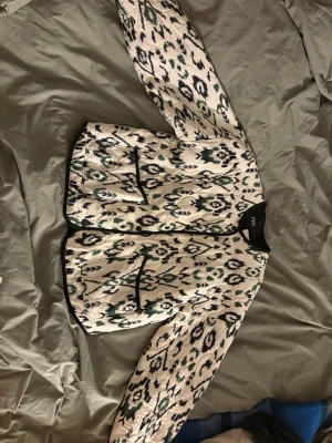 Mönstrad cardiganjacka från Zara - Snygg cardiganjacka från Zara med svart, vit och grön grafiskt mönster. Jackan har svarta kanter, två framfickor och rund halsringning. Perfekt för att lyfta din outfit med en unik touch. Materialet känns mjukt och passar bra till lager-på-lager. Använt en gång. Skriv för fler frågor
