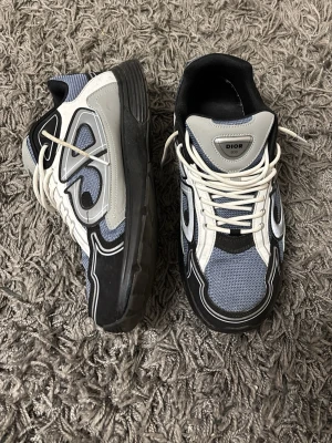  sneakers i svart och grå -  sneakers med mesh och läderdetaljer i svart, grått, vitt och blått. Skorna har chunky sula, vita snören och coola kontrastpaneler. Perfekta för dig som gillar streetwear och exklusiva märken.