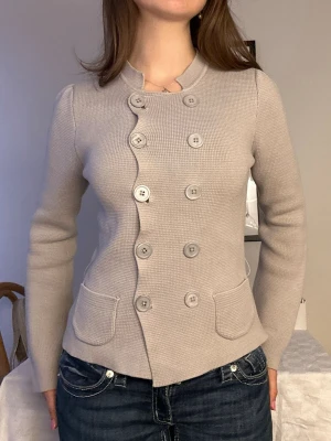 Ljusgrå kofta med dubbla knapprader🩶 - Snygg ljusgrå kofta med unik vågig knäppning och dubbla rader stora knappar framtill. Koftan har två fickor fram, lång ärm och är tillverkad i ett mjukt, stickat material. Perfekt för dig som gillar stilrena och moderna plagg. Knappt använd!🩶