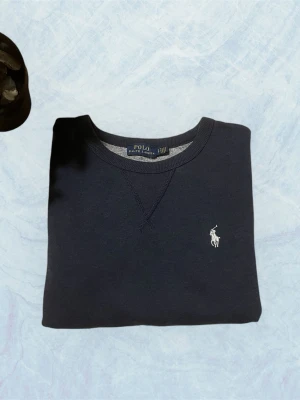 Mörkblå sweatshirt från Polo Ralph Lauren - Klassisk mörkblå sweatshirt från Polo Ralph Lauren med rund halsringning och broderad vit logga på bröstet. Tröjan har ribbade muddar vid ärmslut och nederkant samt en avslappnad passform. Perfekt för en stilren och enkel look. Liten xs! Har några fläckar!