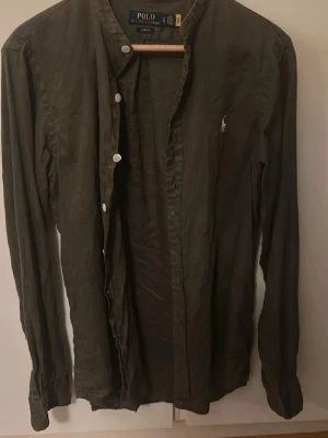 Olivgrön skjorta från Polo Ralph Lauren - Säljer denna snygga olivgröna skjortan från Ralph Lauren. Skjortan har vita knappar och långa ärmar. Tillverkad i en mjuk och tunt bomull som är skön mot huden och blir perfekt till sommaren ☀️ 🏝️ 