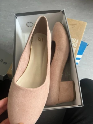 Beigea pumps med blockklack från din sko  - Snygga pumps från XIT i beige mockaimitation med rundad tå och stabil blockklack. Skorna har en stilren design och är perfekta för dig som gillar klassiska men trendiga detaljer. Klacken är bred och ger bra stöd. Passar till många olika outfits.