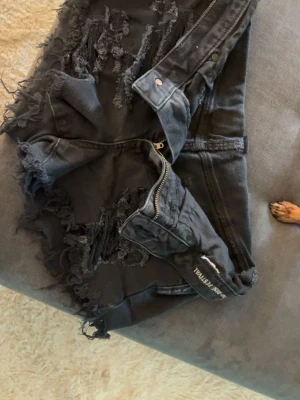 Svarta jeansshorts från American Eagle - Säljer ett par svarta jeansshorts från American Eagle i storlek xs/s med slitna detaljer och fransade kanter. Shortsen har hög midja, dragkedja och klassiska fickor både fram och bak. Perfekta för en avslappnad och trendig sommarstil.