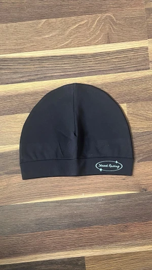 Svart Street Racing mössa - Säljer en svart mössa från Street Racing med logga i vitt och turkost framtill. Mössan är tillverkad i ett mjukt och stretchigt material, perfekt för dig som vill ha en enkel och stilren look. Passar både till vardags och när du vill hålla dig varm utomhus.