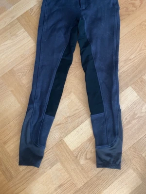 Mörkblå ridleggings med förstärkning - Säljer ett par mörkblå ridleggings med svarta förstärkningar på insidan av benen och vid knäna. De har en tajt passform och är perfekta för dig som gillar att rida eller vill ha ett par leggings med extra stöd.