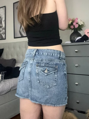 Blå jeanskjol  - Säljer en blå jeanskjol i kort modell med rå kant nertill och snygga detaljer framtill. Kjolen har fickor bak med knapp och klassisk jeanslook. Perfekt till sommaren och enkel att matcha med olika toppar❤️