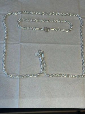 Äkta silver halsband 925 och armband  - Säljer ett äkta halsband och armband 925 Silver i flätad design med silverfärg. Halsbandet har en tvinnad kedja och rund bricka vid låset. Passar perfekt för dig som gillar klassiska accessoarer med en modern twist.