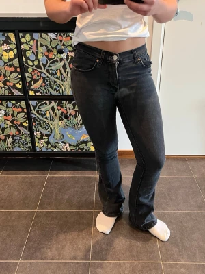 Svarta raka jeans med låg midja - Säljer ett par svarta jeans med rak passform och låg midja. Jeansen har klassiska fem fickor, silverfärgade nitar och knapp, samt vita sömmar längs benen. Perfekta för en avslappnad och trendig look.