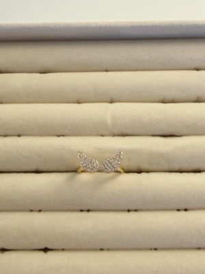 Guldfärgad ring med vingar  - Unik guldfärgad ring med två vingar dekorerade med små gnistrande stenar. Ringen har en öppen design och vingarna är tätt satta med klara stenar som ger ett lyxigt intryck. Perfekt för dig som gillar detaljer och vill sticka ut.