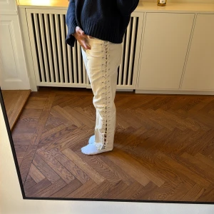 Vita jeans med snörning i sidan - Unika vita jeans med cool snörningsdetalj längs hela utsidan av benen. Rak passform och hög midja ger en trendig siluett. Perfekta för dig som vill sticka ut och addera något extra till din outfit.