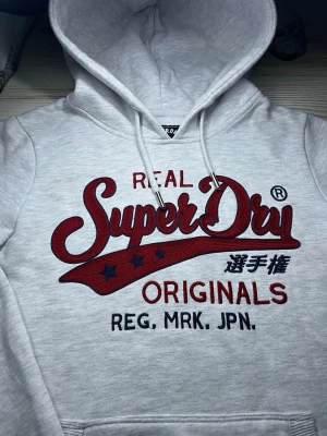 vit Superdry hoodie med tryck - säljer denna feta superdry hoodie i vit med rött tryck på bröstet🤩Inga fel och passar S🙌🏻 Hör av er vid snabbaffär samt funderingar😇