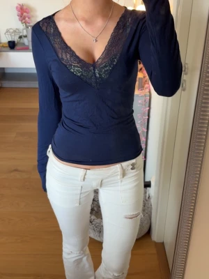 Mörkblå topp med spets - Snygg mörkblå långärmad topp från Gina Tricot med djup v-ringning och dekorativ spetsdetalj framtill. Figurnära passform som framhäver siluetten