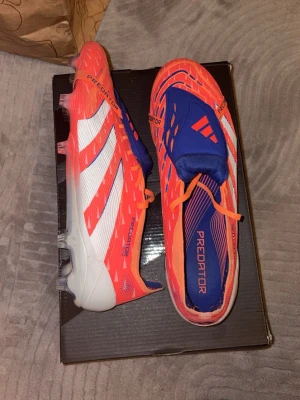 Adidas Predator orange/blå fotbollsskor - Säljer ett par Adidas Predator fotbollsskor i en riktigt snygg orange och blå färg med vita detaljer. Skorna har klassiska tre ränder på sidan, låg profil och snörning. Ovandelen är i syntetmaterial och sulan har dobbar för bra grepp på planen. Perfekta för dig som vill sticka ut på matchen! De är använda endast 1 gång. Har dessvärre ingen original box eller påse då jag fick de av min klubb som de var. Kan gå ned vid snabb affär och är öppen till eventuella byten.