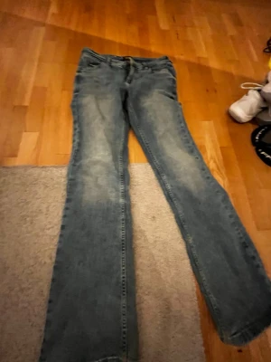 Blå raka jeans med slitningar - Säljer ett par klassiska blå jeans med lite utsvängda ner till och snygga ljud blåa knän  framtill. Jeansen har fem fickor och normal midja. Perfekta till en avslappnad stil och passar till det mesta. Materialet är denim i bomull 
